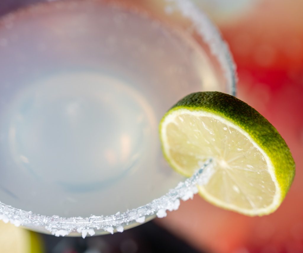 Nahaufnahme eines Margarita-Glases mit Salzrand und Limettenscheibe, leicht verschwommener Hintergrund.