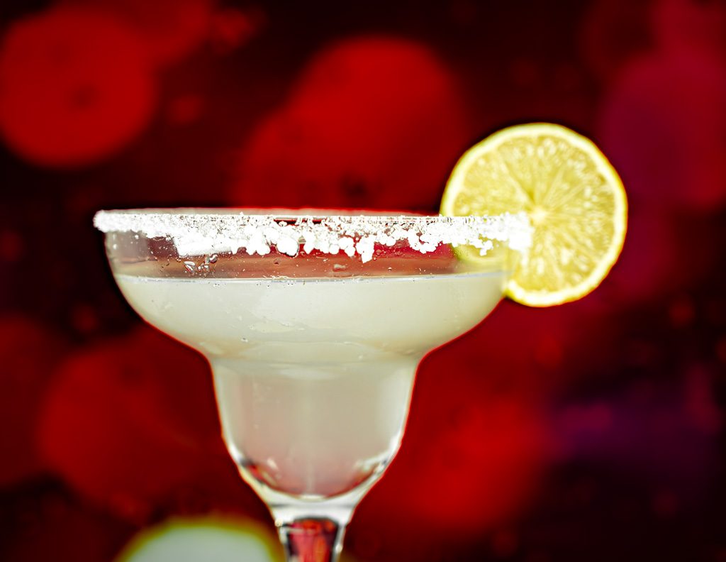 Klassischer Margarita-Cocktail mit gesalzenem Glasrand und Limettenscheibe vor rotem Hintergrund.