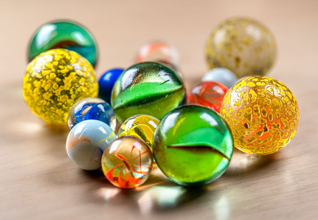 World Marbles Day – Welt-Murmel-Tag. Kuriose Feiertage – immer am Karfreitag © 2024 Sven Giese – Bild 2 Verschiedenfarbige Glasmurmeln liegen locker verteilt auf einer hellen Holzfläche.