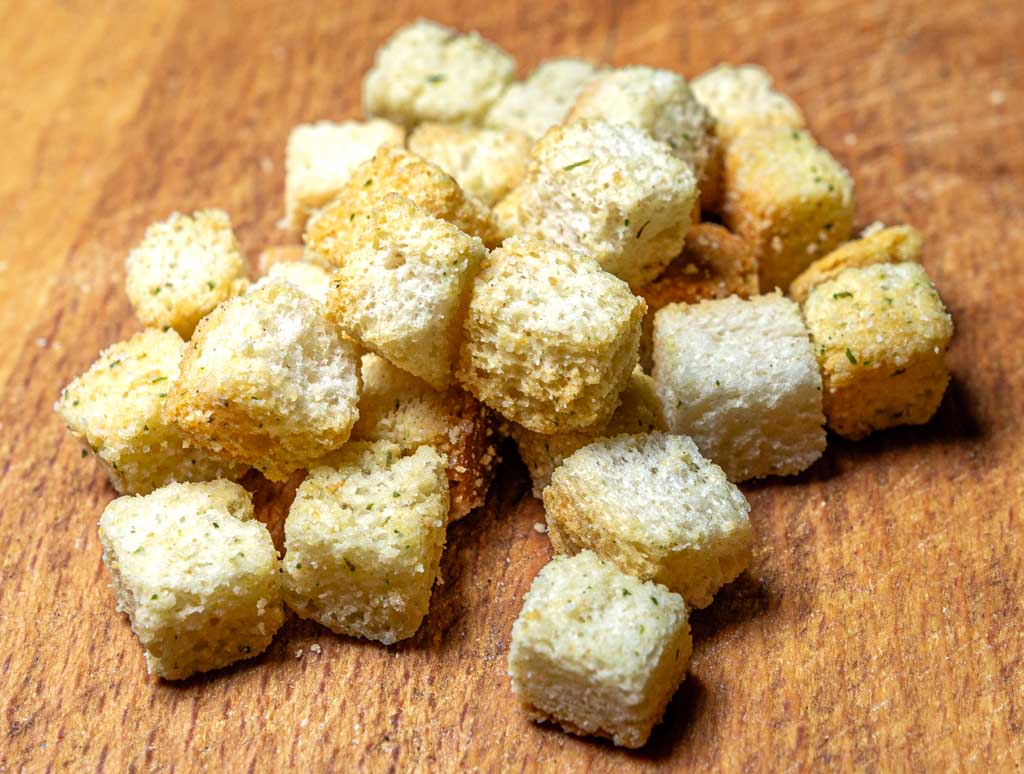 Gewürzte Croutons aus Weißbrot liegen auf einem hölzernen Schneidebrett gestapelt.
