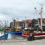 Fischerboote im Hafen mit roten Dächern im Hintergrund und zwei Bronzefiguren im Vordergrund
