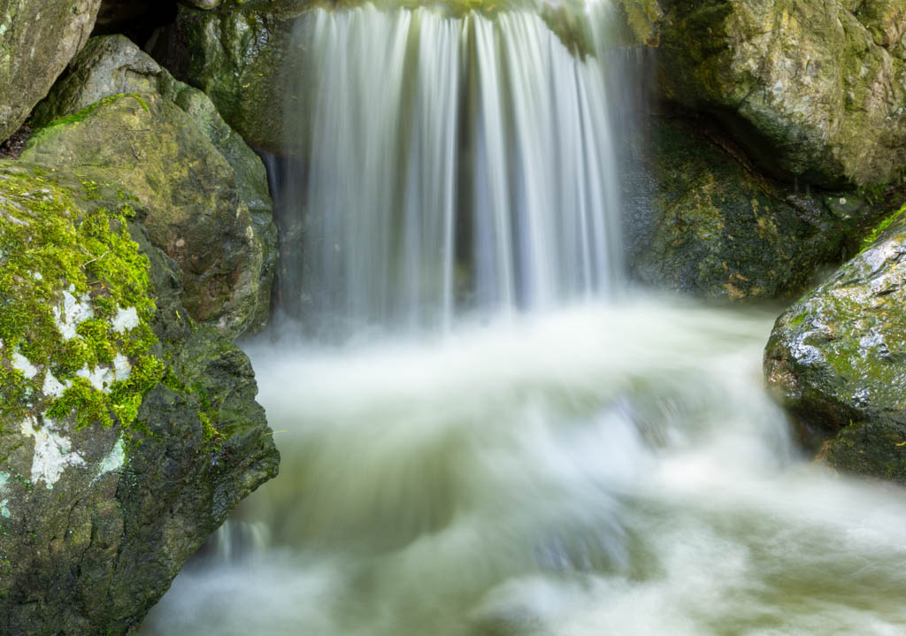 Breiter Wasserfall, der sanft über Felsen in ein ruhiges Becken fließt.