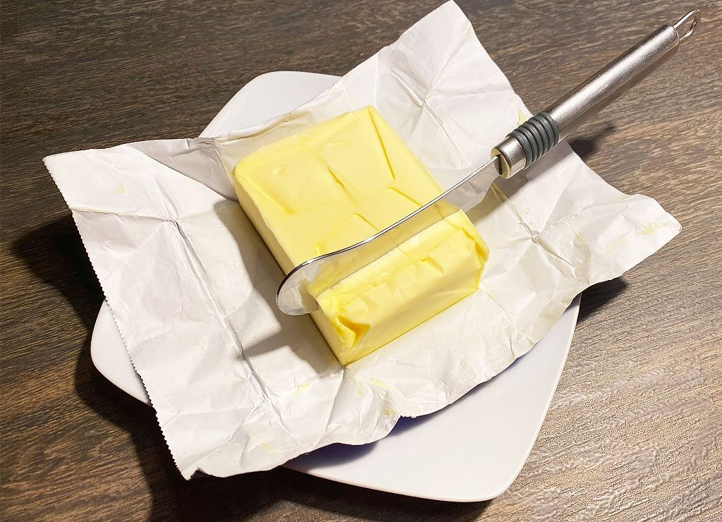 Butterblock auf Papier, mit einem Buttermesser zum Schneiden, auf einem Teller angerichtet.