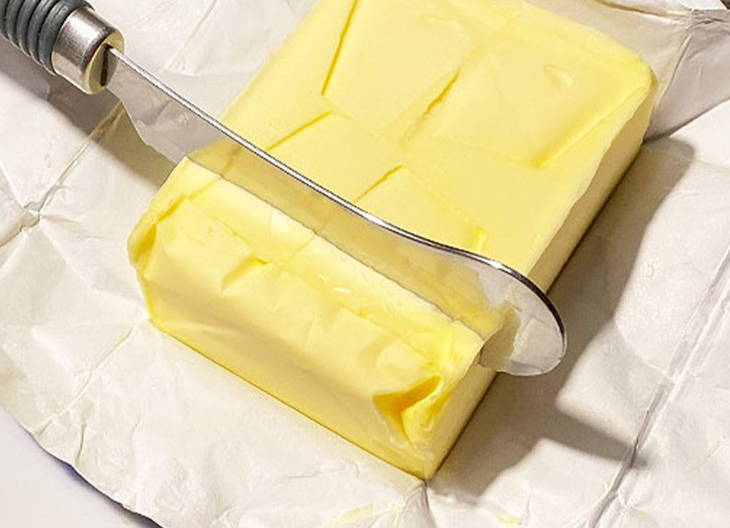 Nahaufnahme eines Butterblocks mit einem Buttermesser zum Schneiden.