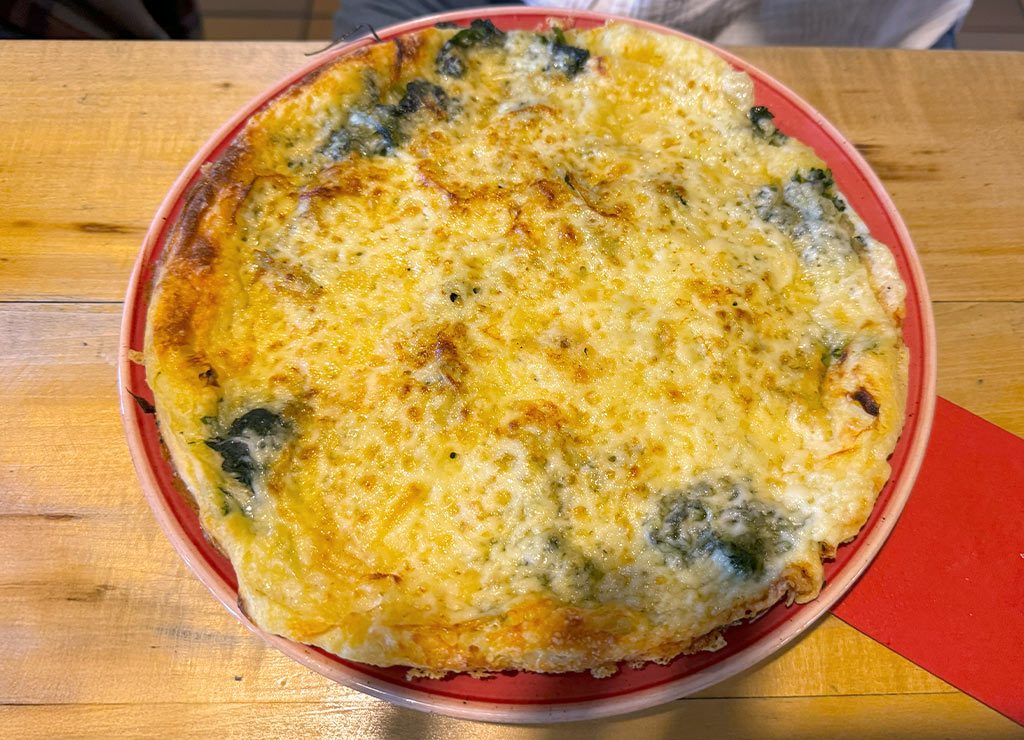 Goldbraune Pizza mit überbackenem Käse und angedeutetem Gemüse darunter.
