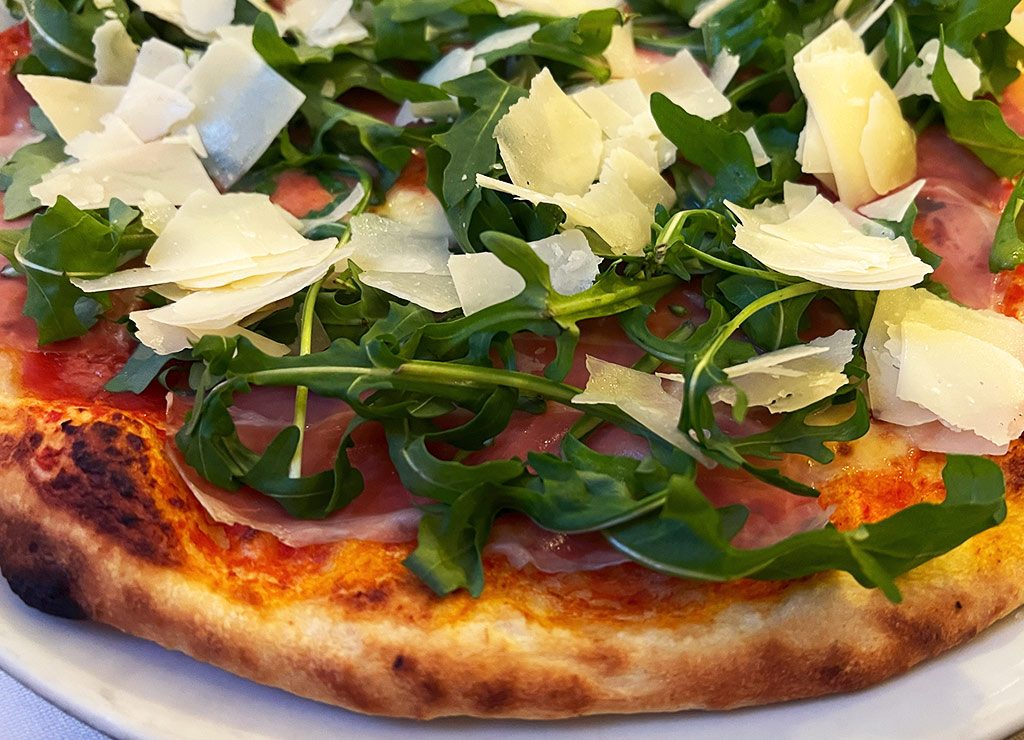 Frische Pizza belegt mit Rucola, Schinken und gehobeltem Parmesan auf knusprigem Boden.