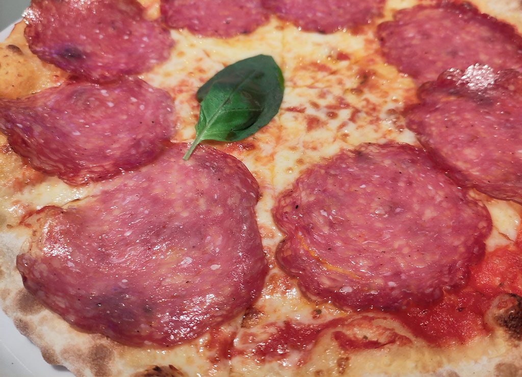 Nahaufnahme einer Pizza mit großer Salami und einem Basilikumblatt in der Mitte.