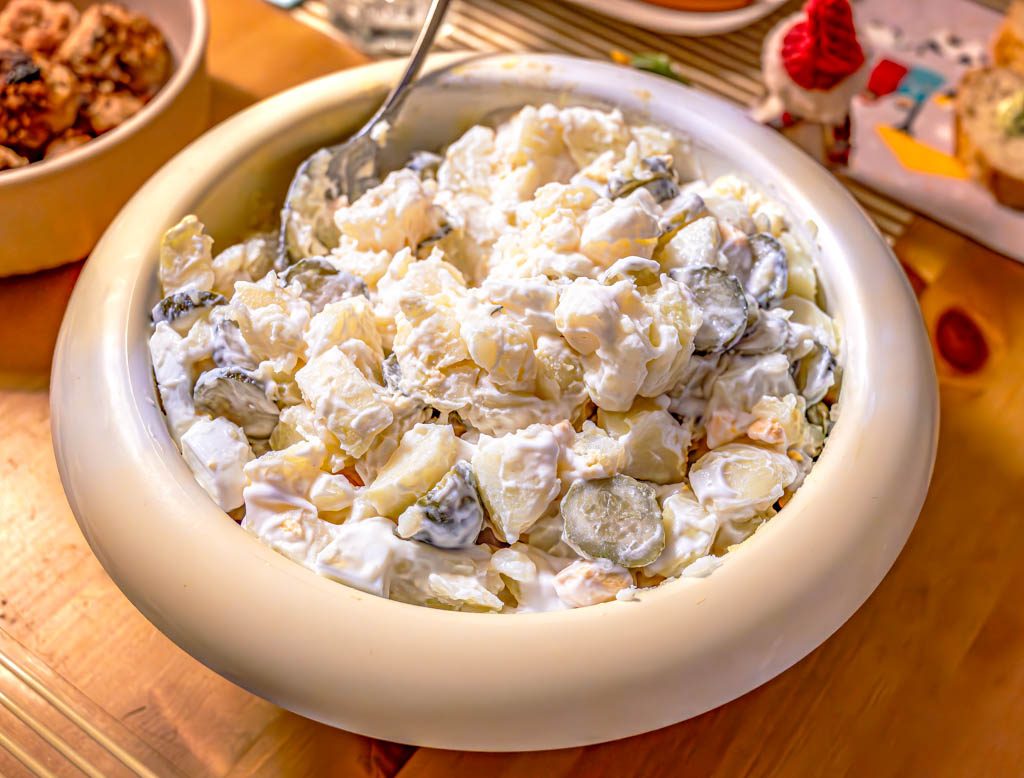 Große weiße Schüssel mit Kartoffelsalat, darin Gurkenstücke und cremige Mayonnaise-Sauce.