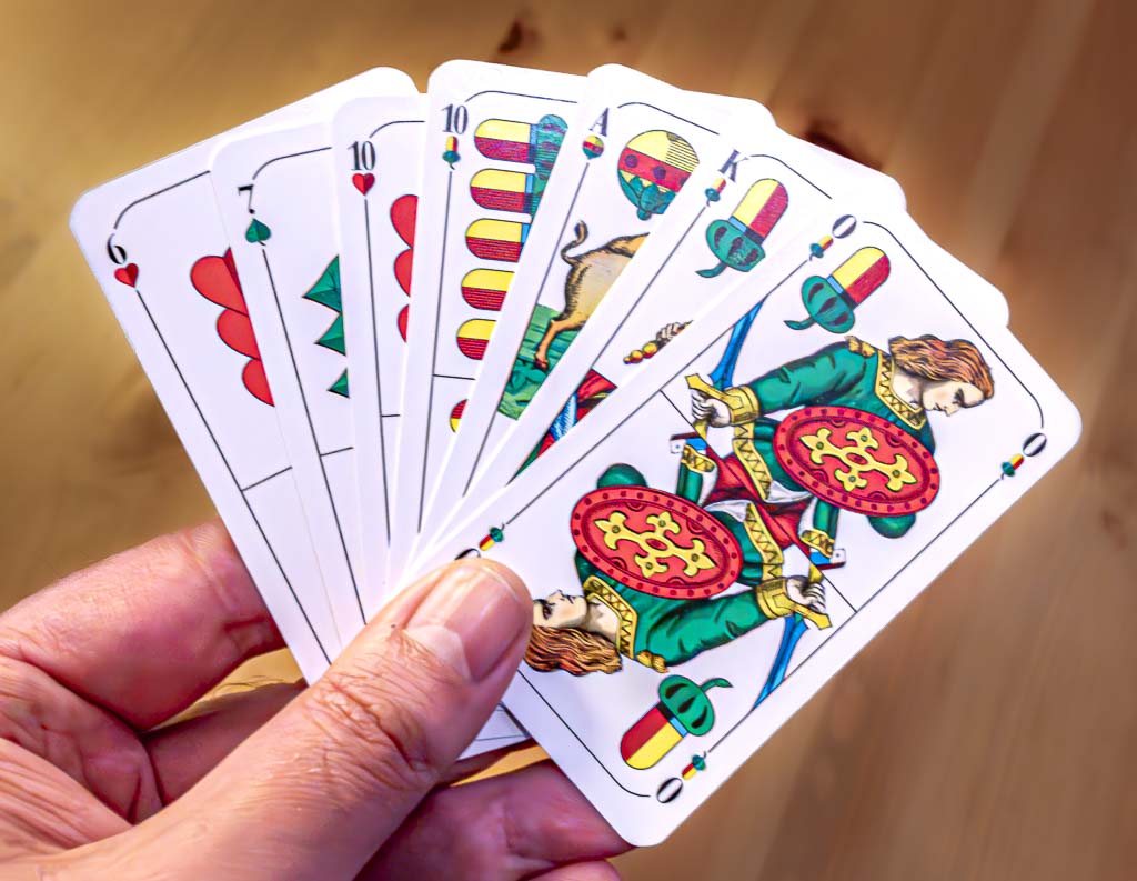 Weltschafkopftag. Kuriose Feiertage - 12. Januar © 2025 Sven Giese. Hand hält Spielkarten eines deutschen Kartendecks im Schafkopf, darunter Könige, Zehner und Siebener.