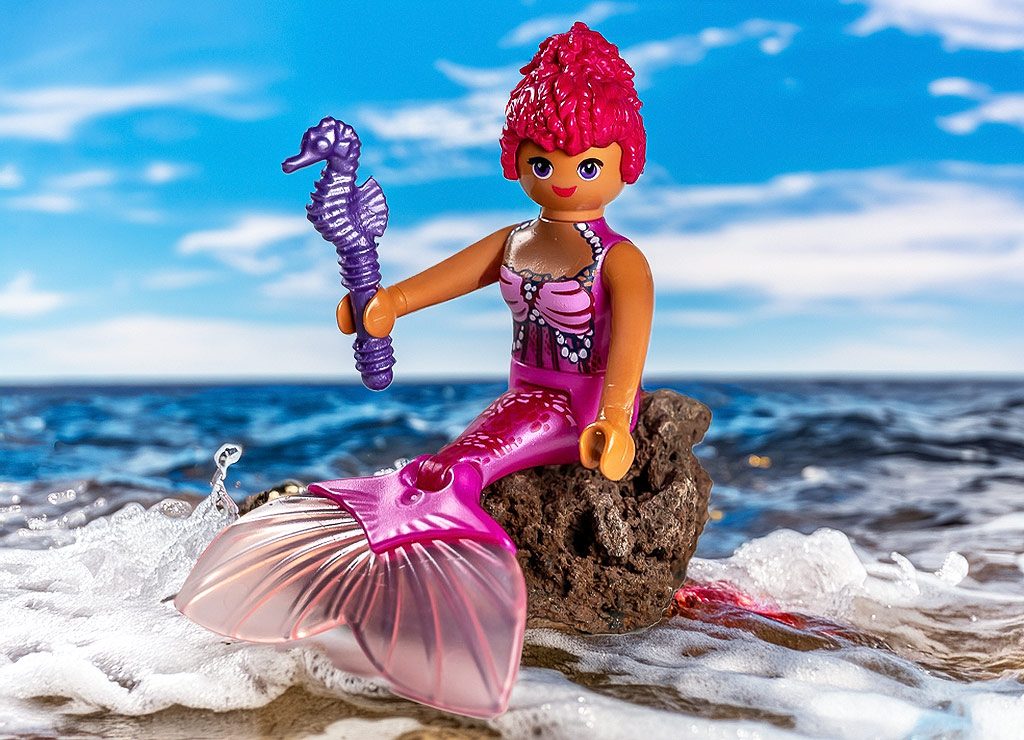 Internationaler Tag der Meerjungfrauen – International Mermaid Day. Kuriose Feiertage - 29. März © 2025 Sven Giese Playmobil-Meerjungfrau mit pinker Flosse sitzt auf einem Felsen am Meer und hält ein Seepferdchen.
