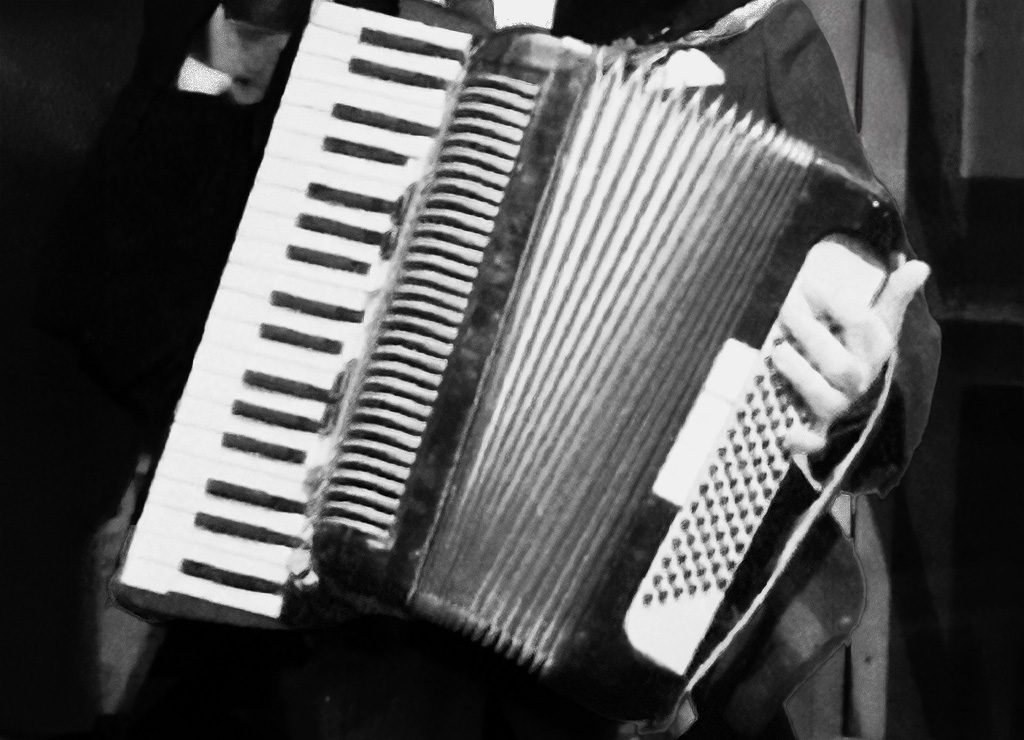 Nahaufnahme eines Akkordeonspielers in Schwarz-Weiß, Hände auf Tasten und Knöpfen des Instruments.