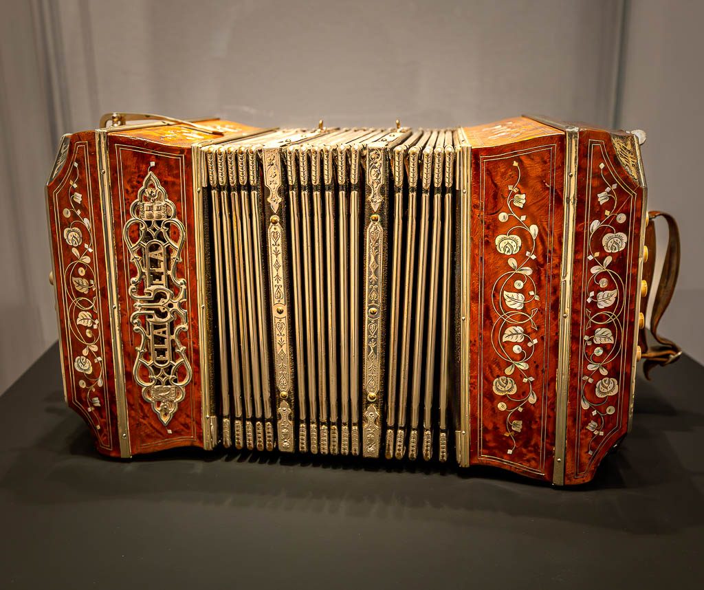 Día del Bandoneón – Tag des Bandoneons in Argentinien. Kuriose Feiertage 11. Juli © 2025 Sven Giese – Bild 3 Bandoneon mit verziertem Gehäuse und goldenen Zierleisten frontal auf schwarzem Tisch.