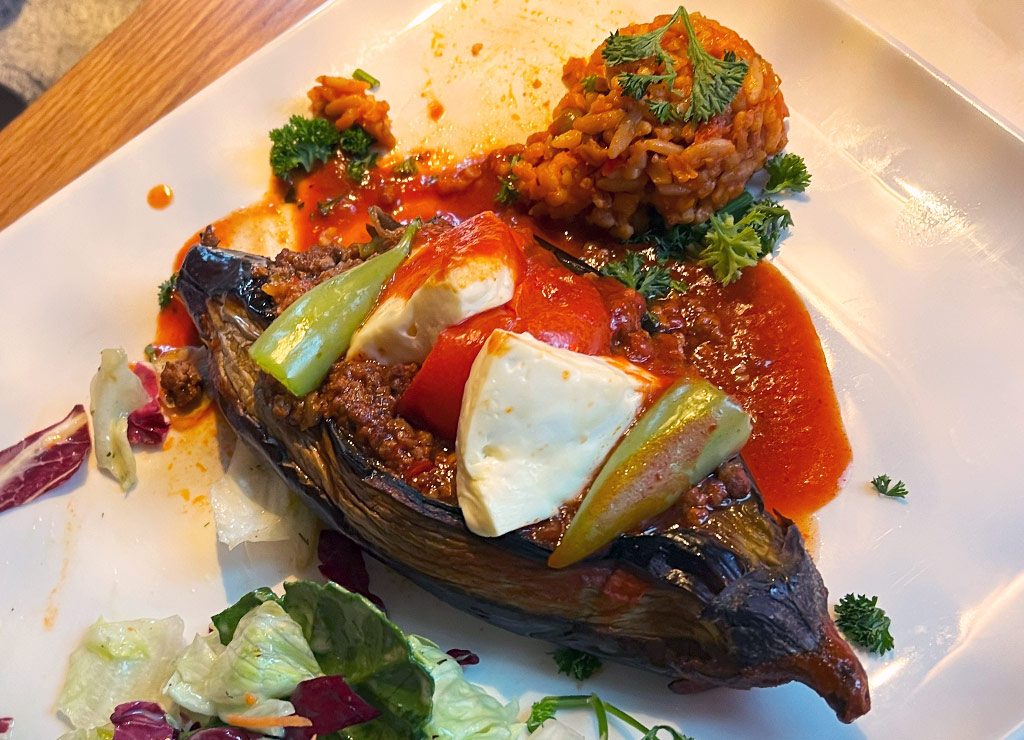 Gefüllte Aubergine mit Hackfleisch, Gemüse und Käse, serviert mit Reis und Salat.