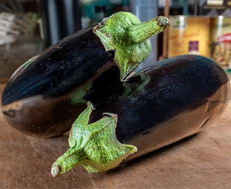 Zwei frische, glänzende Auberginen liegen nebeneinander auf einem hölzernen Küchentisch.