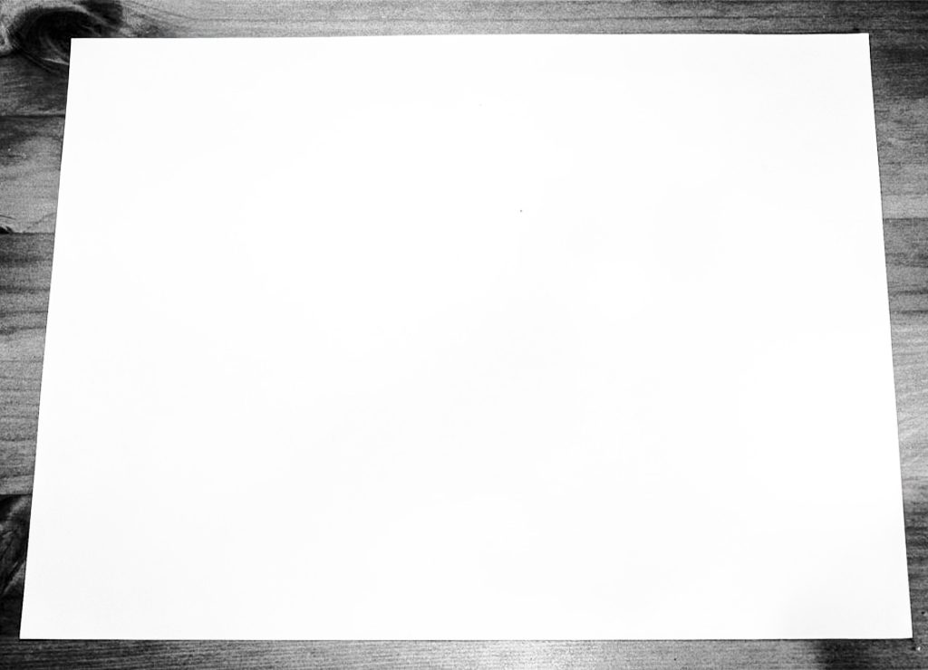 Ein leeres, weißes DIN‑A4‑Blatt Papier im Querformat liegt mittig auf einer hölzernen Tischplatte.