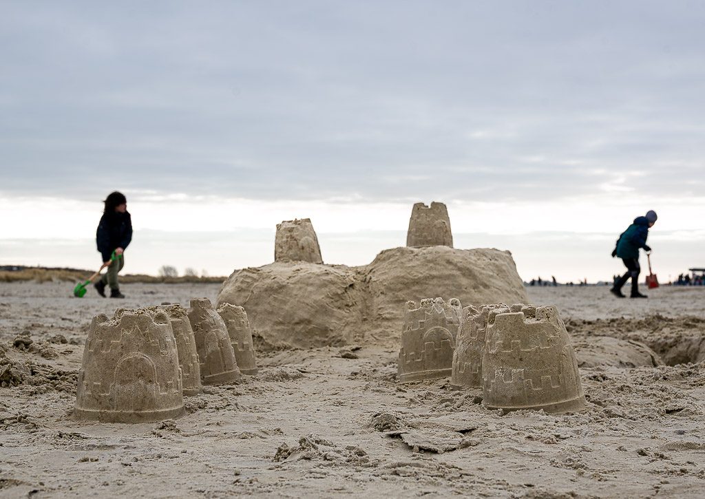 Kinder mit Schaufeln bauen Sandburgen vor bewölktem Himmel am weiten Strand.