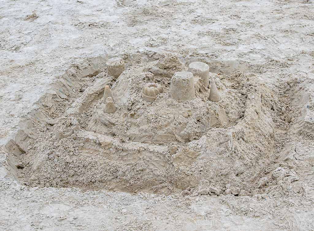 Komplexe Sandburg mit Mauern und Türmen in einer flachen Sandgrube am Strand.
