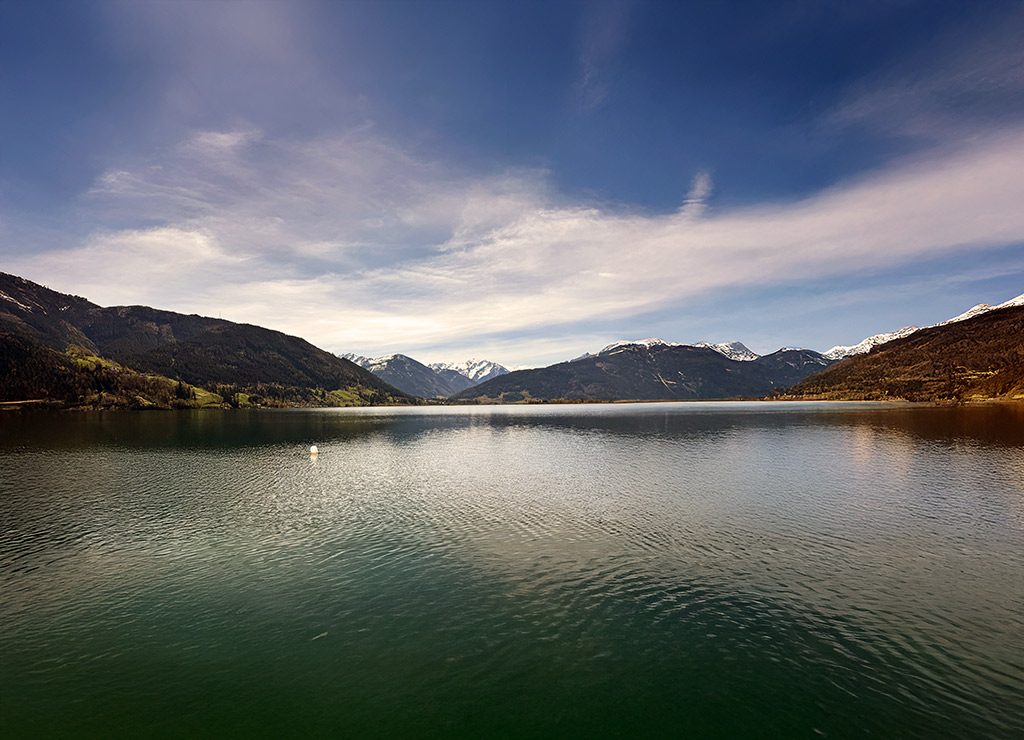Welttag der Seen - UN World Lake Day. Kuriose Feiertage - 27. August (c) 2025 Sven Giese - Bild 1 Weiter Bergsee mit Spiegelung, umgeben von Bergen mit teils schneebedeckten Gipfeln.