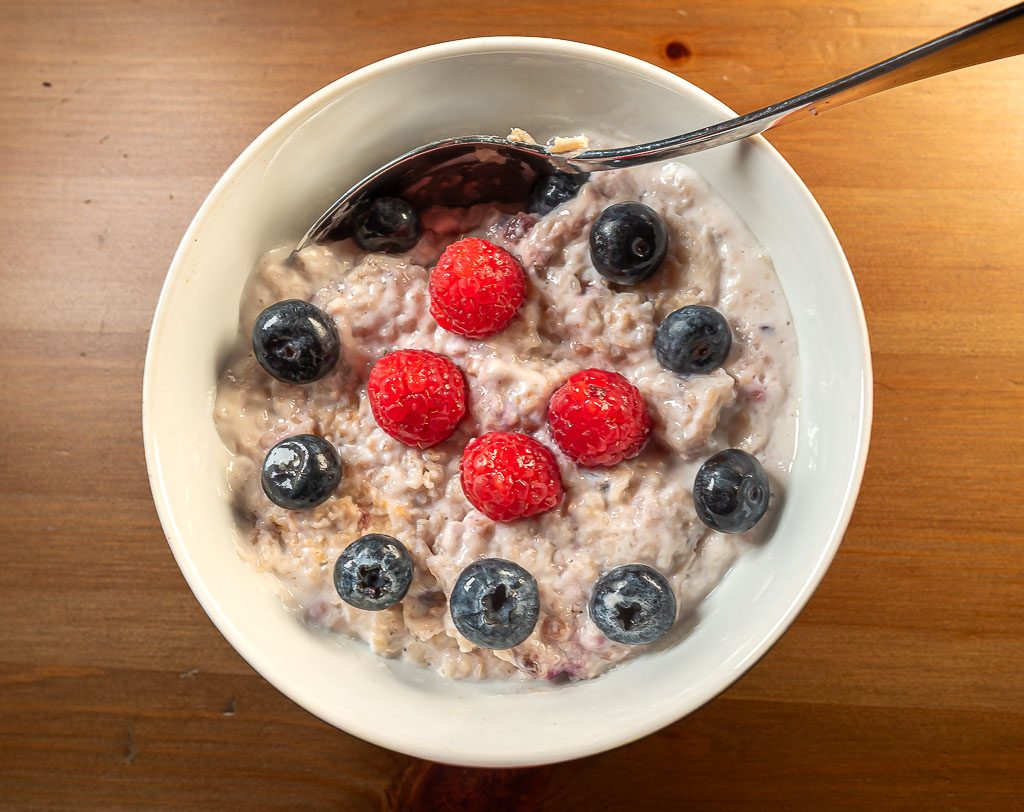 World Porridge Day – Welttag des Porridge. Kuriose Feiertage – 10. Oktober © 2025 Sven Giese - Bild 3 Porridge von oben mit Löffel, Himbeeren und Blaubeeren, cremige Konsistenz auf Holz.
