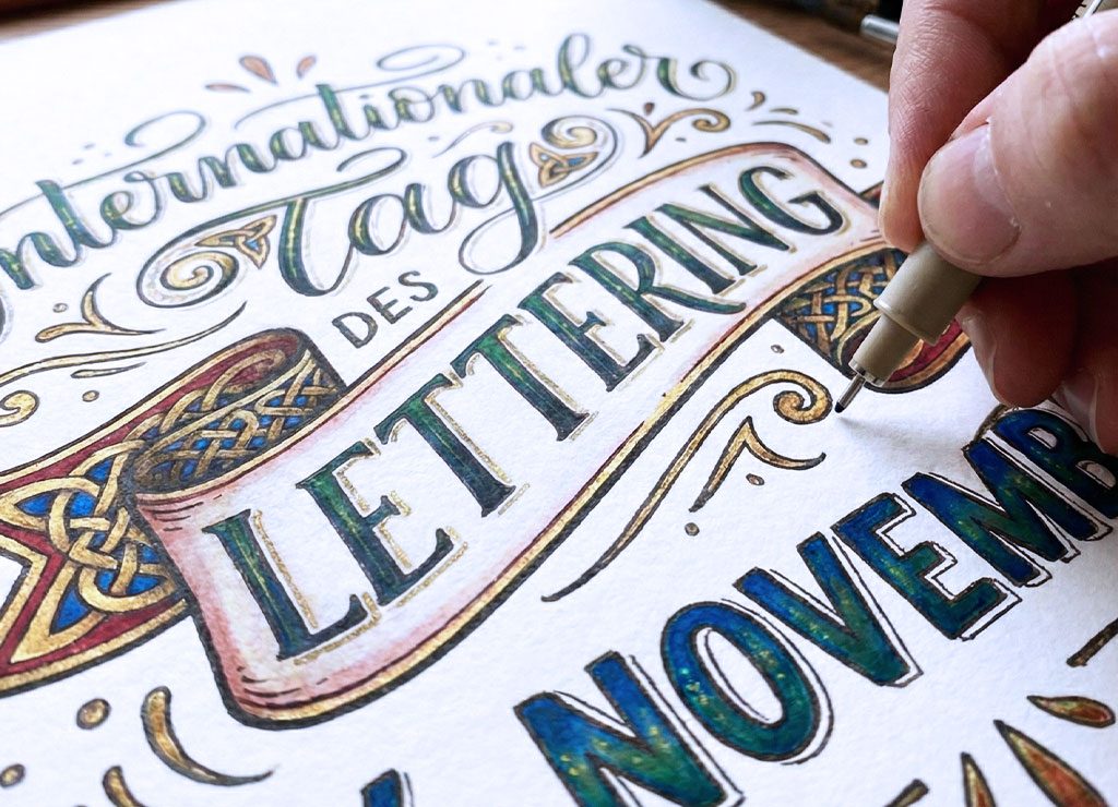 Nahaufnahme einer Hand mit Stift, die ein Lettering-Poster zum Tag des Lettering am 24. November bearbeitet.