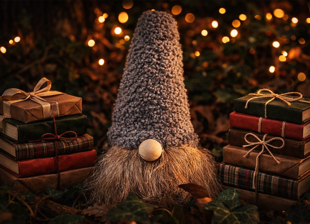 Gnomfigur mit hoher Mütze zwischen gestapelten Büchern, warm beleuchtet von vielen Weihnachtslichtern.