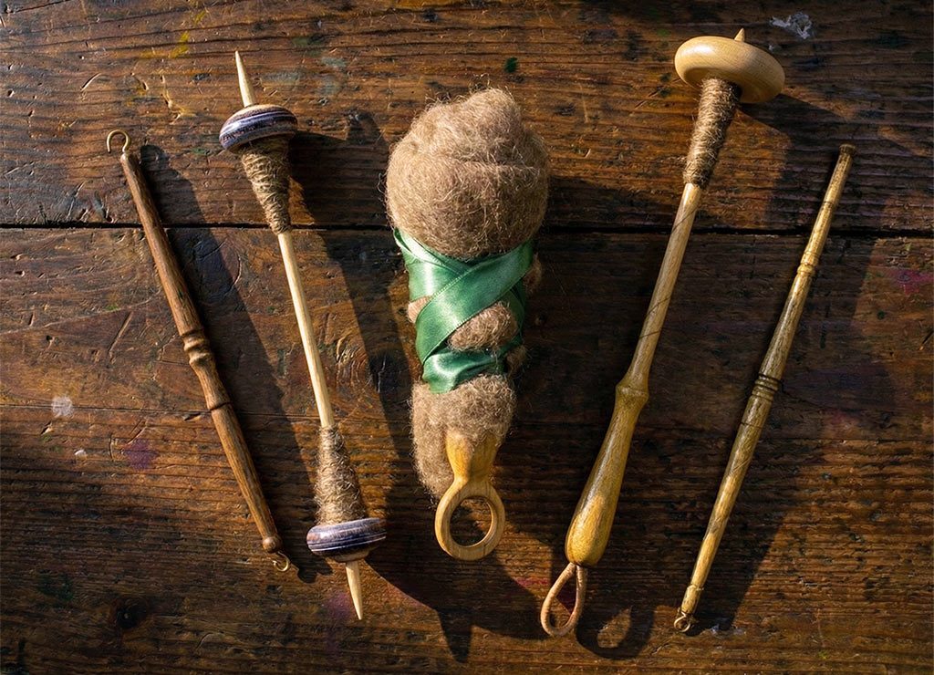 Spinnrocken und aufgewickelte Wolle mit grünem Band liegen geordnet auf rustikalem Holztisch.