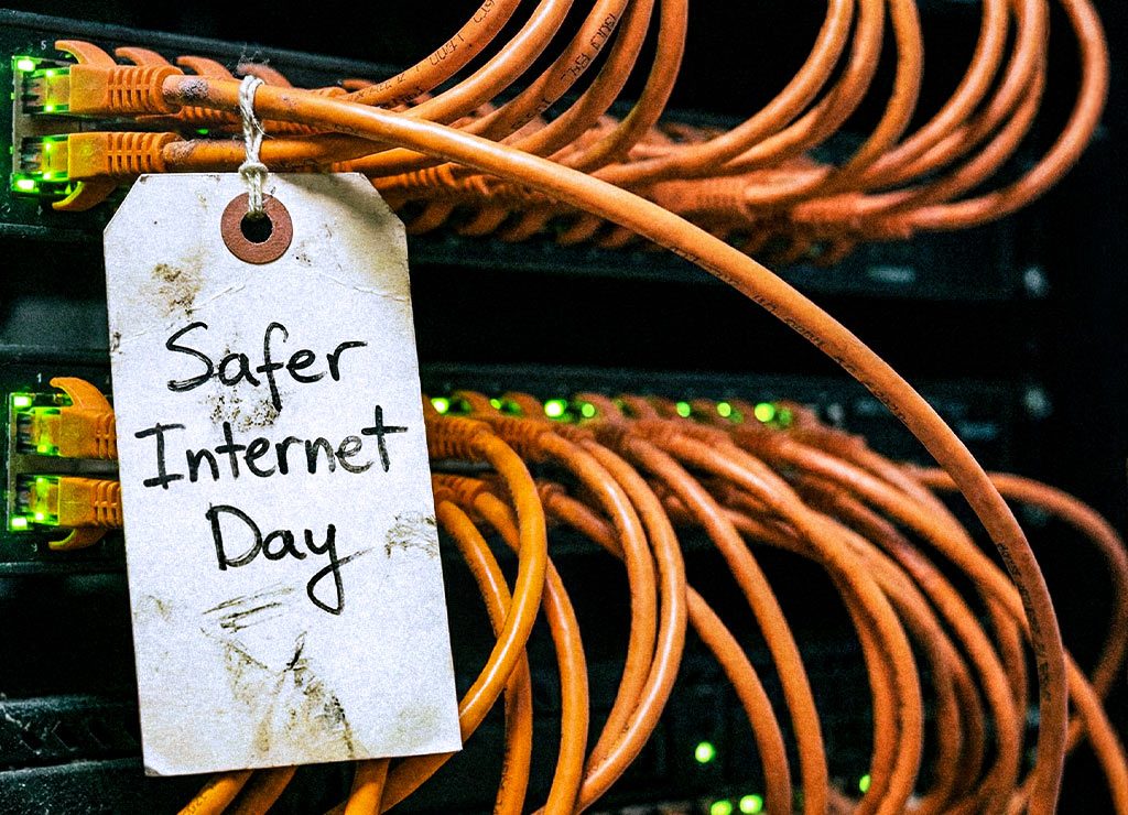 Serverrack mit orangen LAN-Kabeln; Etikett „Safer Internet Day“ hängt davor bei grünen LEDs.