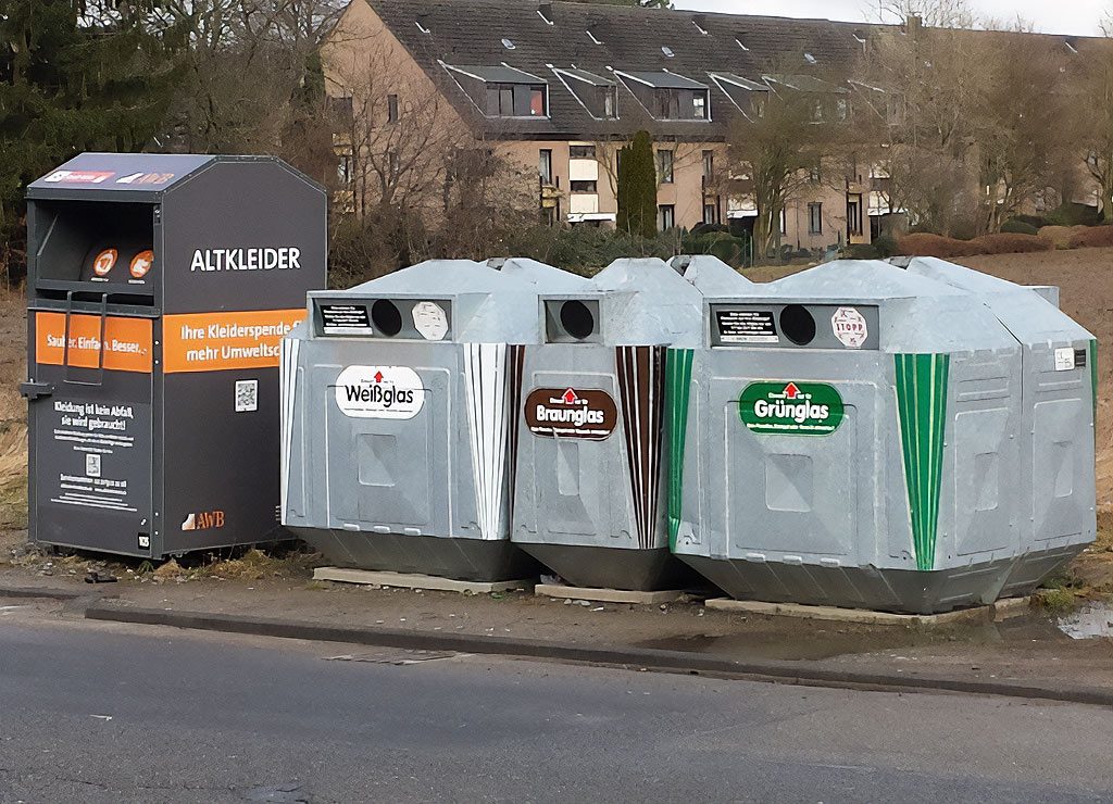 International Day of Zero Waste Day. Kuriose Feiertage - 30. März (c) 2026 Sven Giese - Bild 1 Glascontainer für Weiß-, Braun- und Grünglas neben Altkleiderbox; ruhige Häuserzeile im Hintergrund.