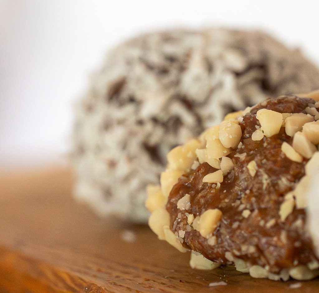 Schokoladenbällchen mit Nussstückchen vorn scharf, Kokoskugel unscharf im Hintergrund.