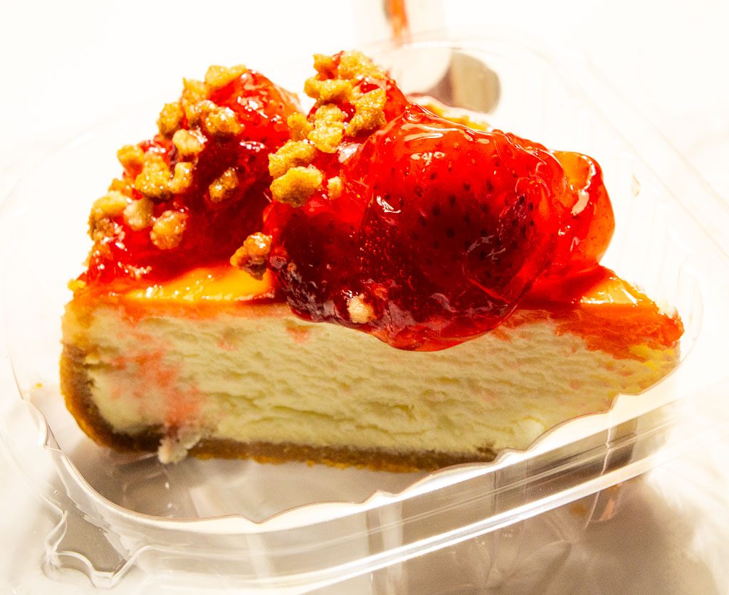 Tag des Erdbeerkäsekuchens – Strawberry Cheesecake Day. Kuriose Feiertage – 8. Juni (c) 2026 Sven Giese – Bild 2 Stück Erdbeerkäsekuchen in Plastikschale, mit glänzenden Erdbeeren und Streuseln.