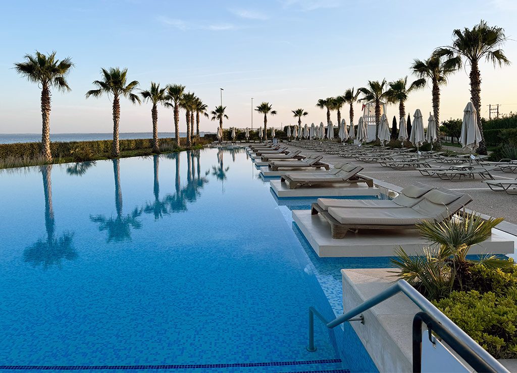Tag des Swimmingpools in den USA – National Swimming Pool Day am 11. Juli (c) 2026 Sven Giese Großer Hotelpool mit Palmen, Liegen und Sonnenschirmen bei ruhigem Abendlicht.