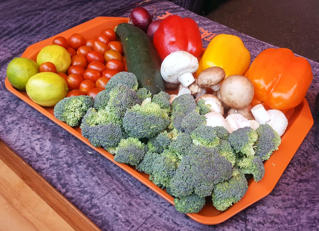 Bunte Auswahl aus Brokkoli, Paprika, Tomaten, Pilzen, Zucchini und Limetten auf einem Tablett.
