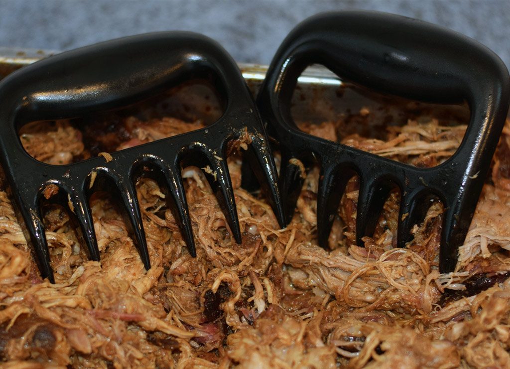 National Pulled Pork Day – der US-amerikanische Tag des Pulled Pork. Kuriose Feiertage – 12. Oktober (c) 2026 Sven Giese – Bild 1 Zwei schwarze Fleischkrallen stecken in zerkleinertem Pulled Pork in einer Bratform.