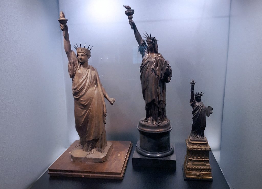 Geburtstag der Freiheitsstatue in New York – Statue of Liberty Dedication Day USA Kuriose Feiertage – 28. Oktober © 2026 Sven Giese – Bild 5 Drei Modelle der Freiheitsstatue in unterschiedlichen Größen stehen in einer beleuchteten Vitrine.