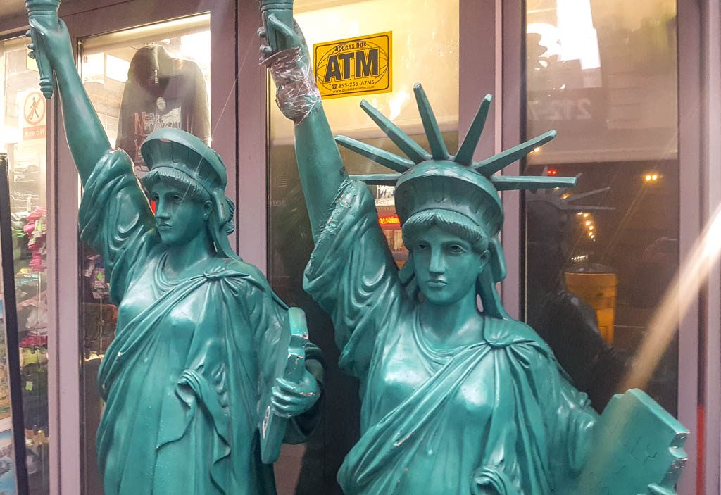 Geburtstag der Freiheitsstatue in New York – Statue of Liberty Dedication Day USA Kuriose Feiertage – 28. Oktober © 2026 Sven Giese – Bild 3 Zwei grüne Nachbildungen der Freiheitsstatue stehen vor einem Laden mit gläsernen Türen.